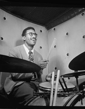 Una foto en blanco y negro de Max Roach tocando la batería.