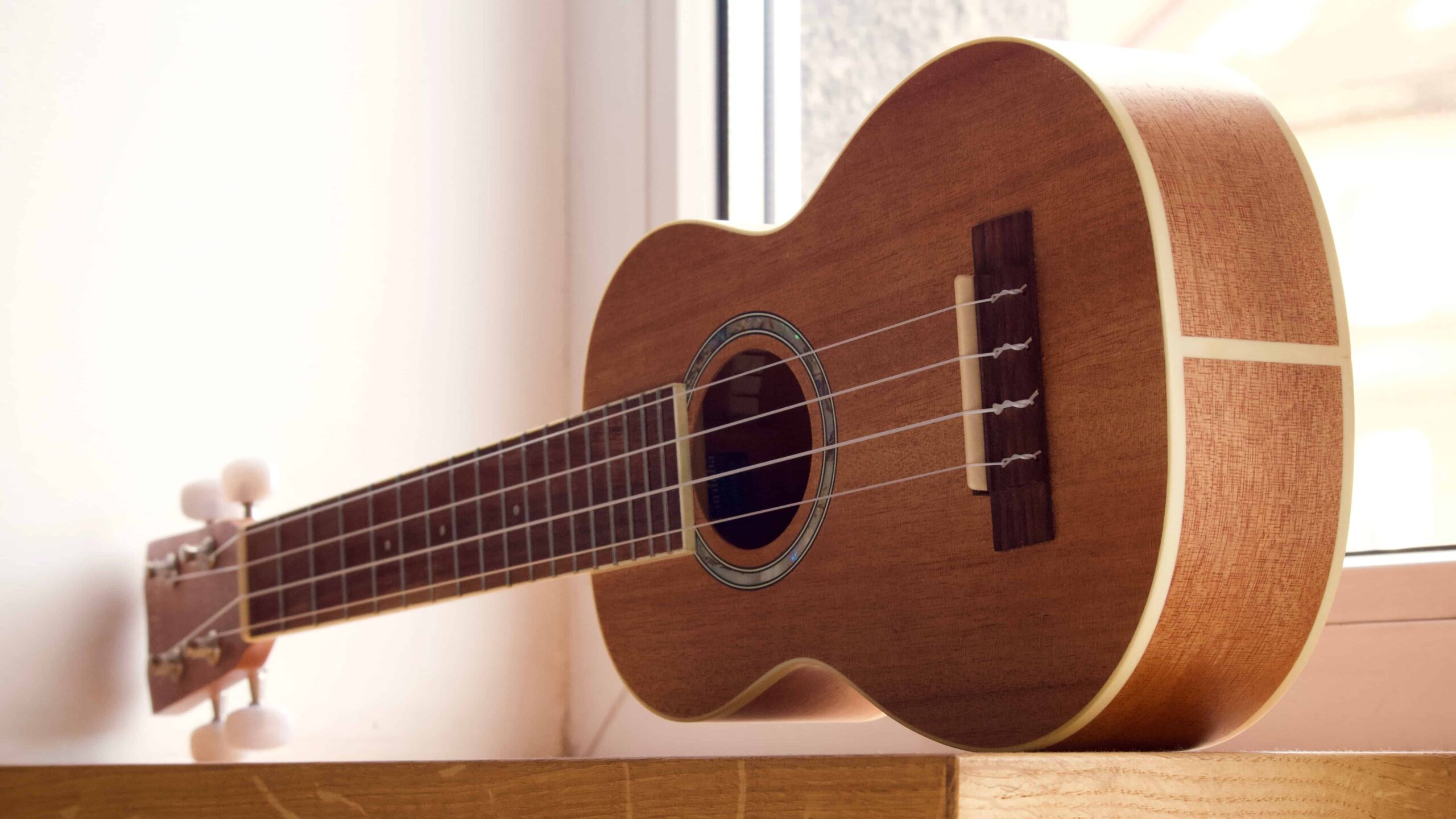Un ukelele marrón cerca de una ventana.