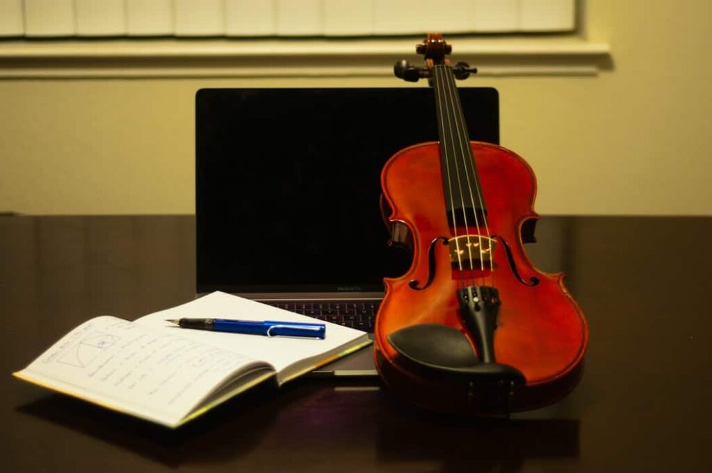 Violín con una computadora portátil y un libro al lado.